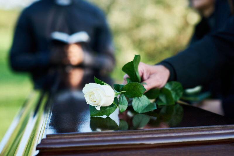 Person placing a white rose on a casket