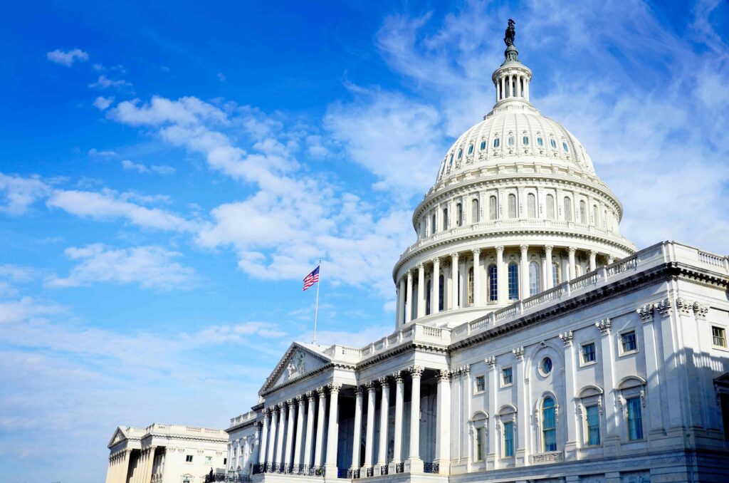United States Capitol building in Washington, DC, with the iconic white dome and American flag under a clear blue sky