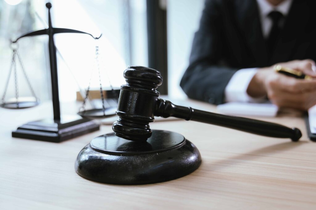Judge’s gavel on a wooden desk with scales of justice and a lawyer writing in the background, symbolizing courtroom proceedings and legal decision-making