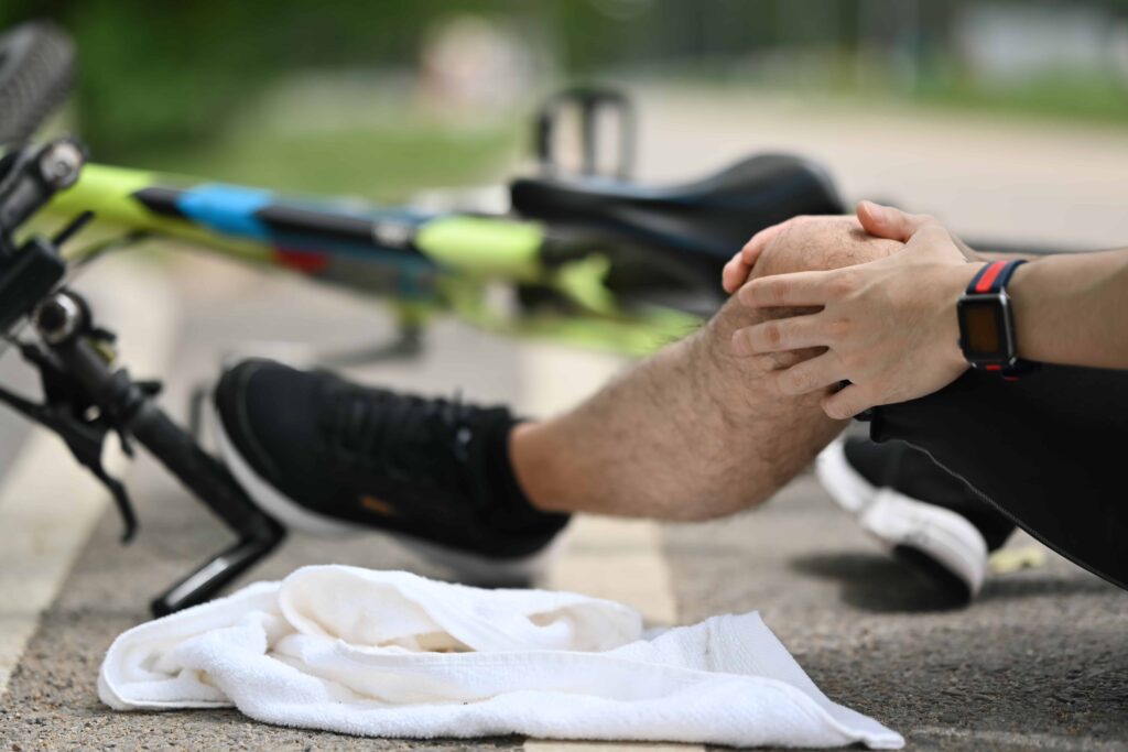 Cyclist sitting on the ground holding an injured knee next to a fallen bicycle, showing a biking accident and knee injury outdoors